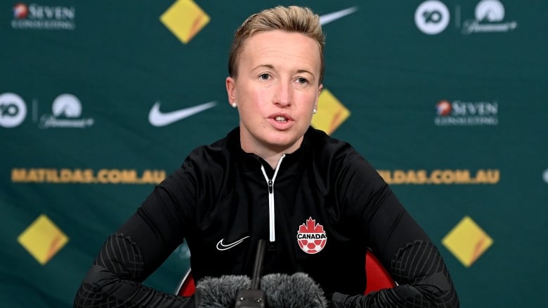 A soccer coach sits in front of a microphone while speaking at a news conference.