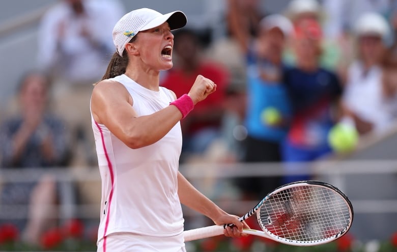 A female tennis player shouts while pumping her right fist in celebration and holding a racket in her left hand.