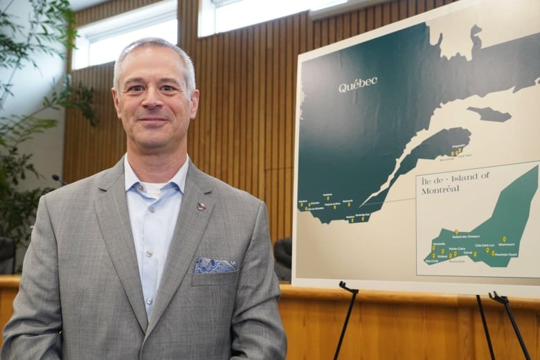A man wearing a suit stands beside a map of Quebec.