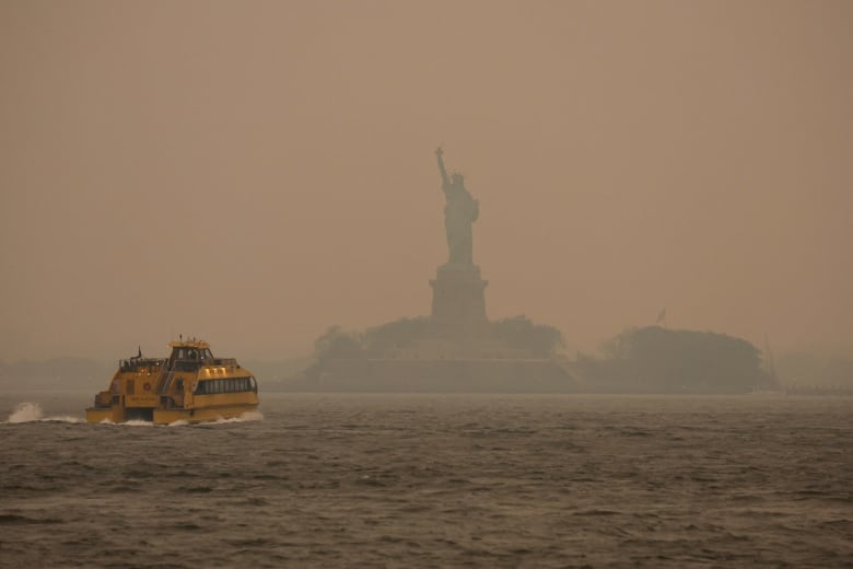 A ferry passing by the Statue of Liberty shrouded in smoky haze due to the wildfires in Canada.