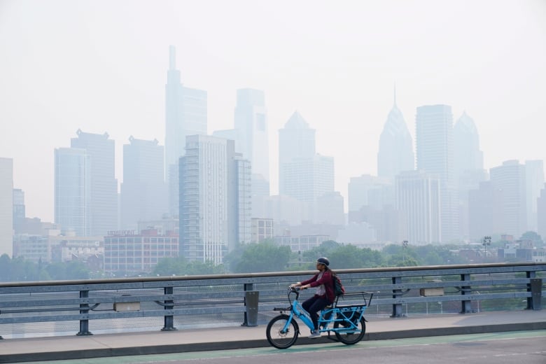 A person on a bicycle is shown in the foreground in front of a grey, hazy city skyline.
