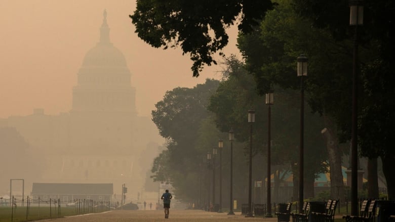 A person is shown at a distance jogging on a path as the U.S. Capitol is shown in the background through a haze.