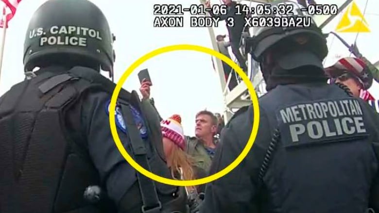 A large yellow circle highlights a person displayed in a still taken from video. In the still, the person is seen between two police officers. 