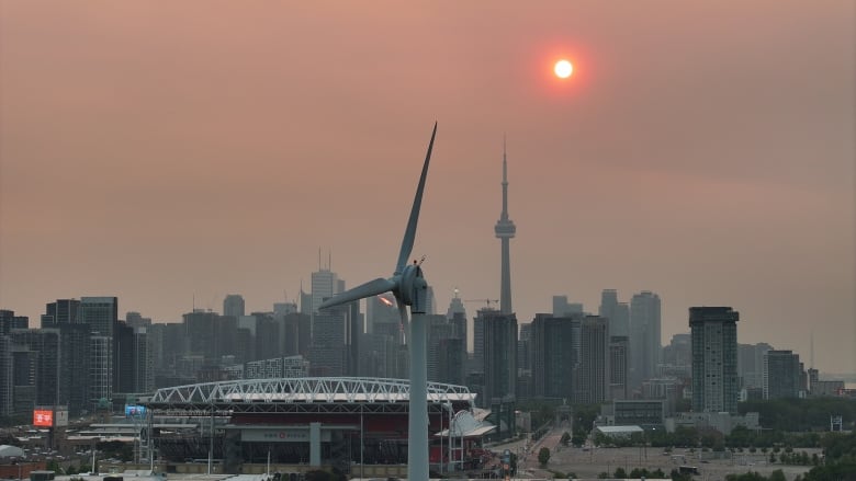 An orange sun rises above the Toronto skyline through a smoky haze. 